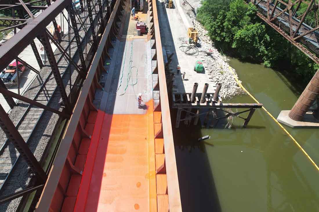 Specialized spray equipment applying waterproofing membrane to bridge deck surface