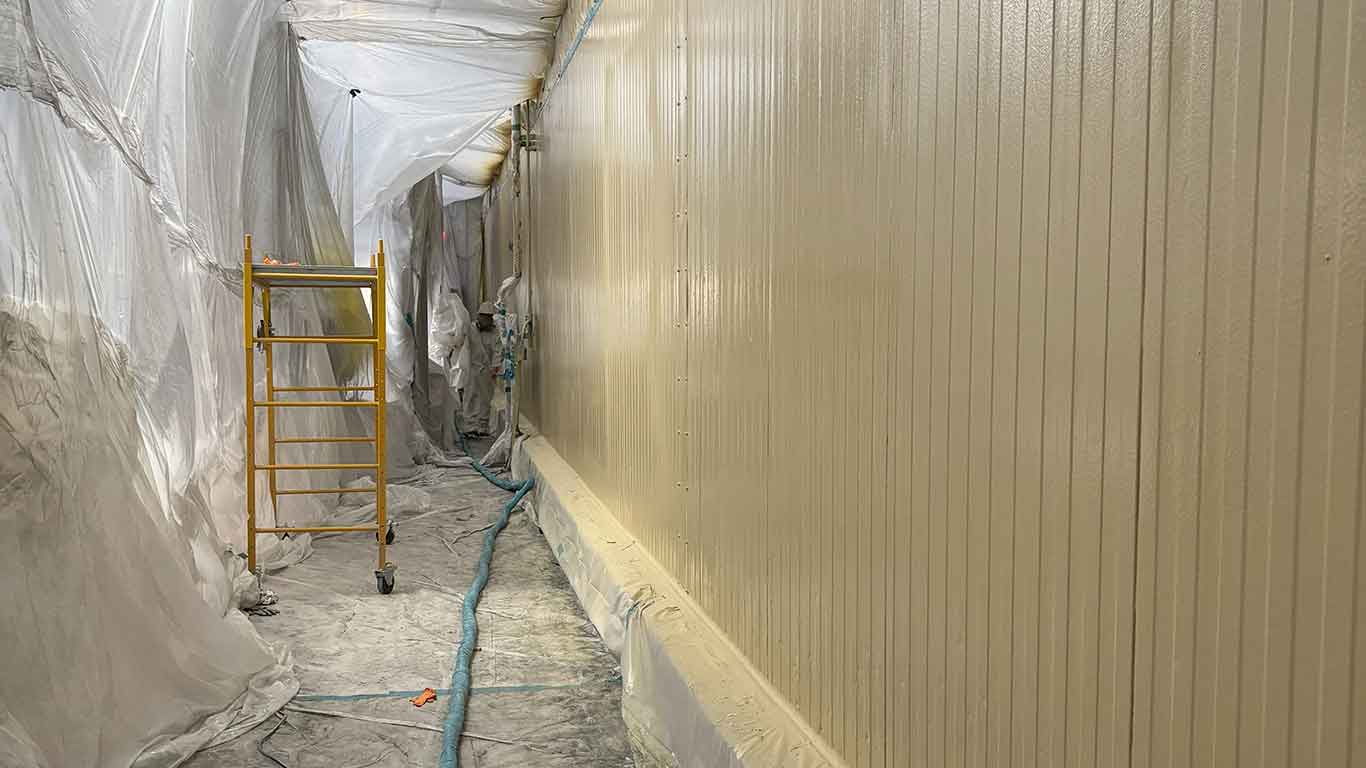 Clean food processing facility showing seamless white polyurea coating application on walls and ceiling with worker in protective gear